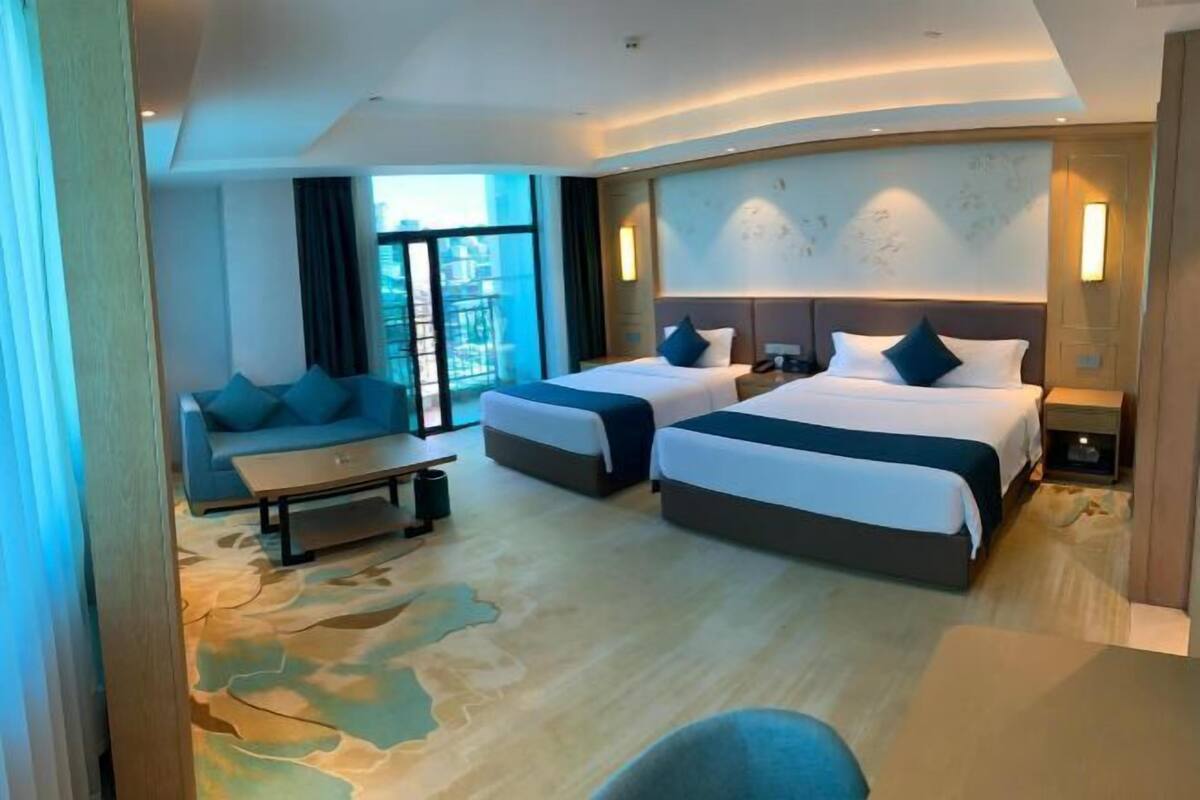 A hotel room with two beds, a sofa, a small table, and a large window.