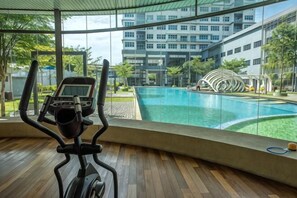 Une salle de sport équipée d’un tapis de course, d’une piscine et offrant une vue sur un immeuble à étages.