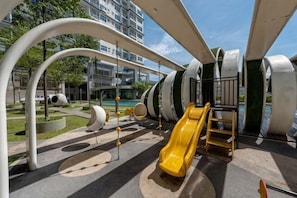 Un parque infantil con toboganes y estructuras para escalar, rodeado de edificios y vegetación.