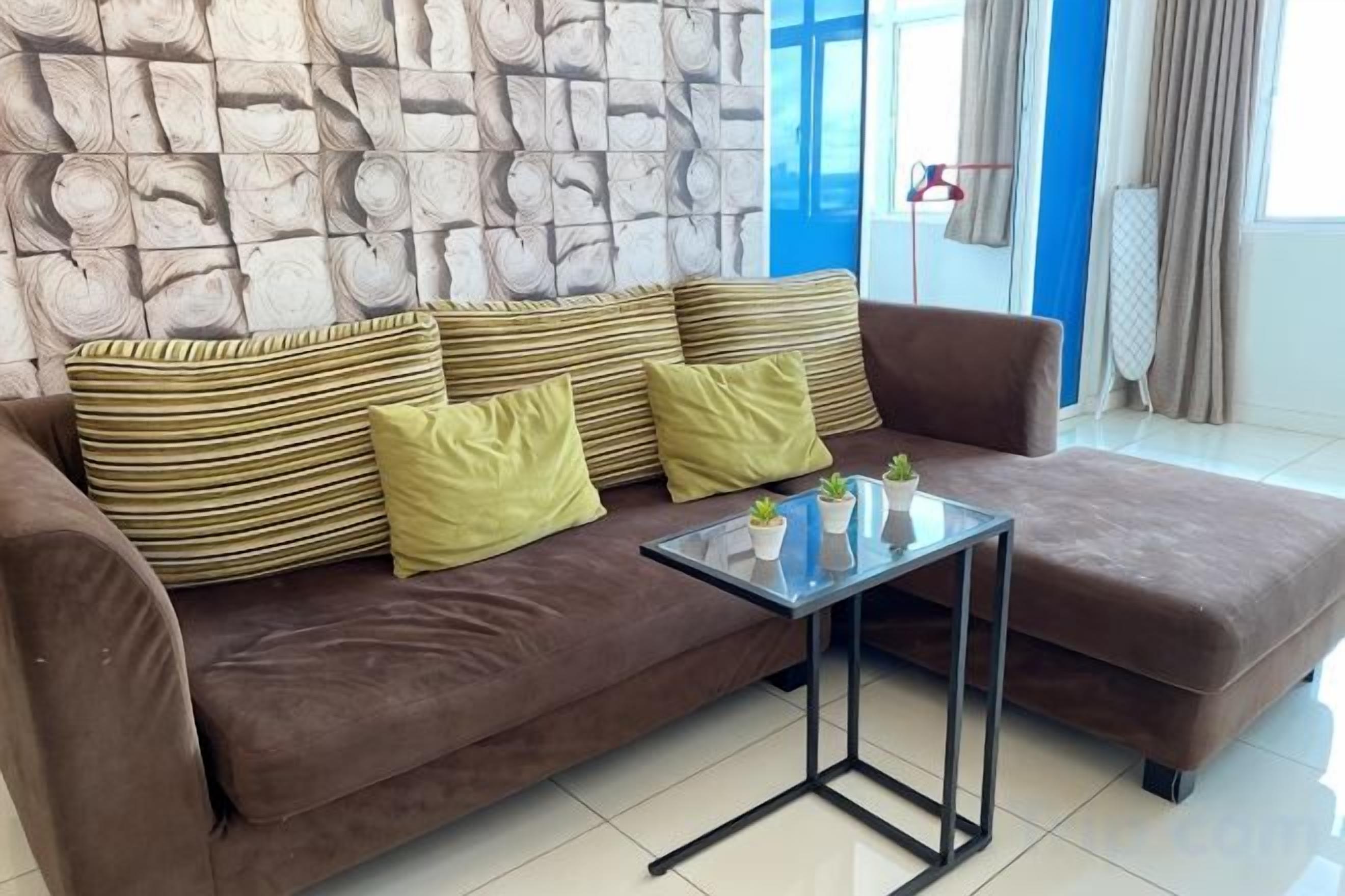 A brown sofa with striped cushions and a glass coffee table in a room with a stone wall and a blue door.