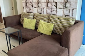 A brown sofa with striped cushions and a glass coffee table in a room with a stone wall. - Comfy Private Home @ Sky.Pod (Puchong)