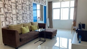 A living room with a brown sofa, a glass coffee table, a TV, and a large window with curtains. - Comfy Private Home @ Sky.Pod (Puchong)
