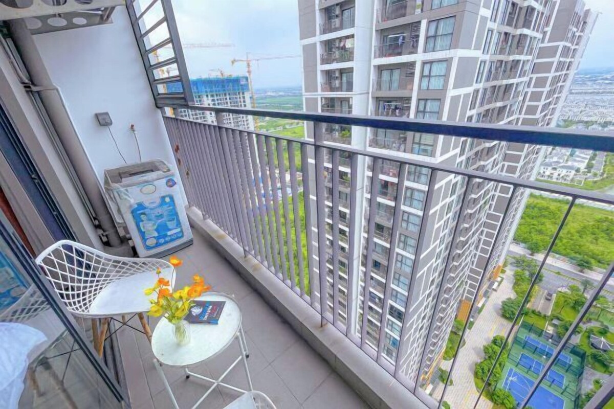 A balcony with a white chair, a small table with a vase of flowers, and a trash bin.