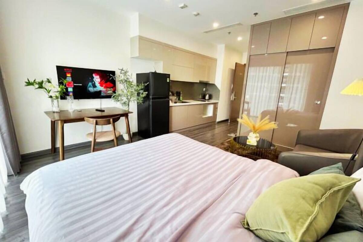 A hotel room with a bed, a desk, a TV, and a kitchenette.