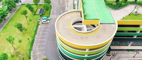 A multi-story parking structure with a circular design, surrounded by greenery and adjacent to a building with a green roof.