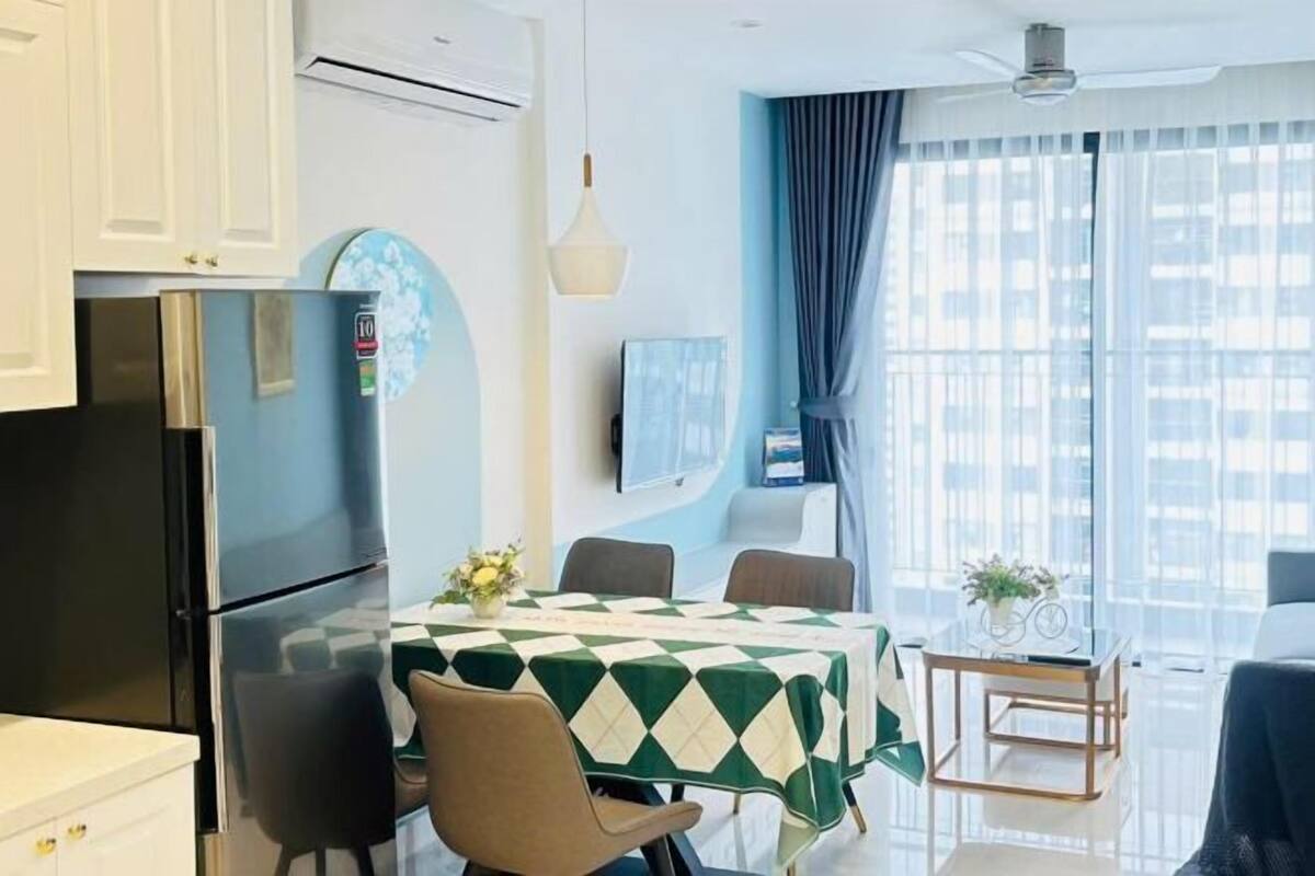 A modern kitchen with a refrigerator, dining table with chairs, and a window with curtains.
