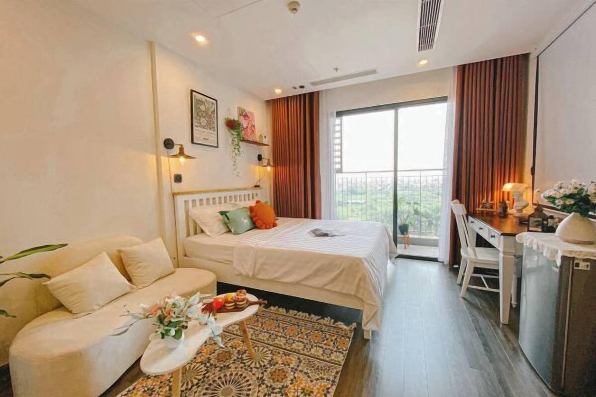 A modern hotel room with a bed, sofa, dining area, and a balcony with a view.
