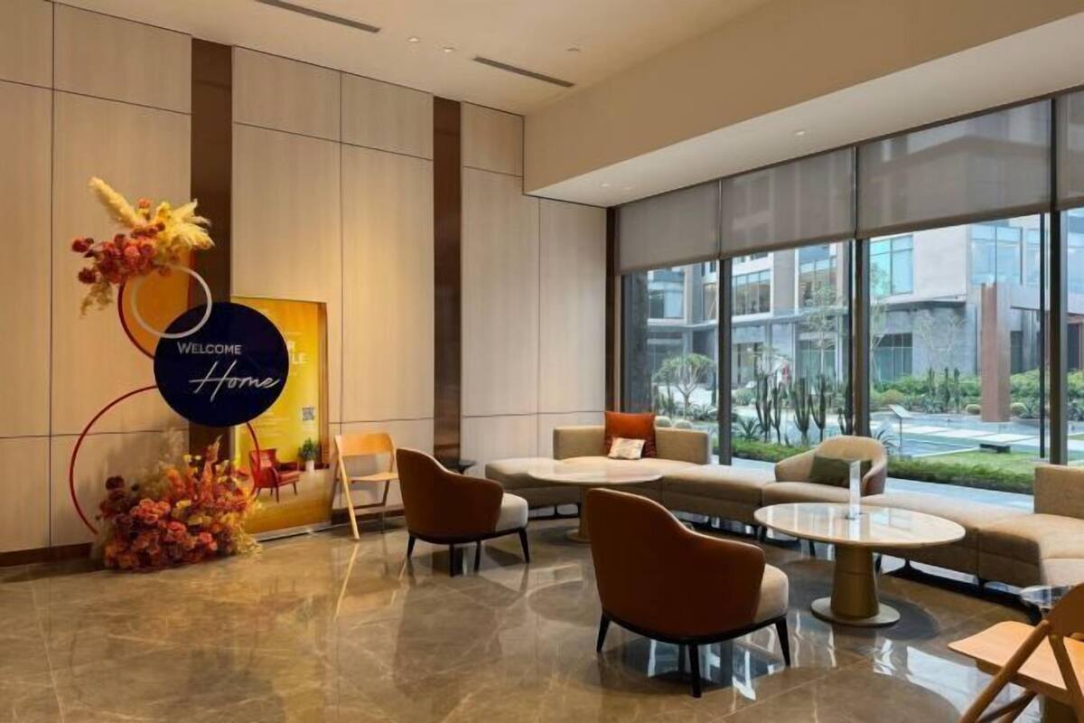 A modern lobby with a 'Welcome Home' sign, comfortable seating, and large windows offering a view of the building's exterior.