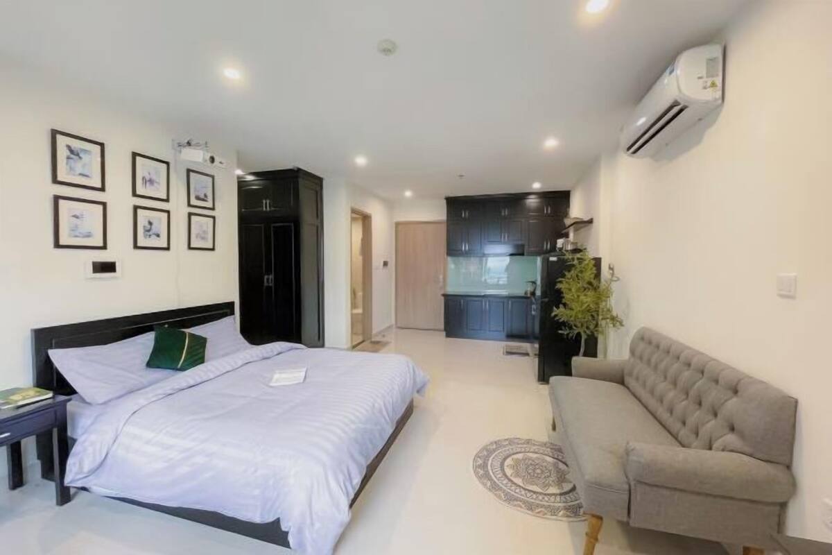 A bedroom with a bed, a bedside table, a sofa, and a small kitchen area.