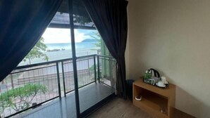 Una habitación con un ventanal grande, un balcón y un pequeño estante de madera con objetos encima.