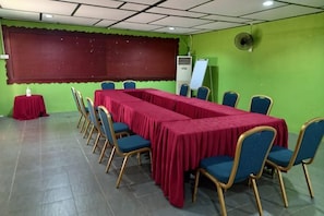 Un salón de conferencias con una larga mesa, sillas, una pantalla de proyector y una pizarra.