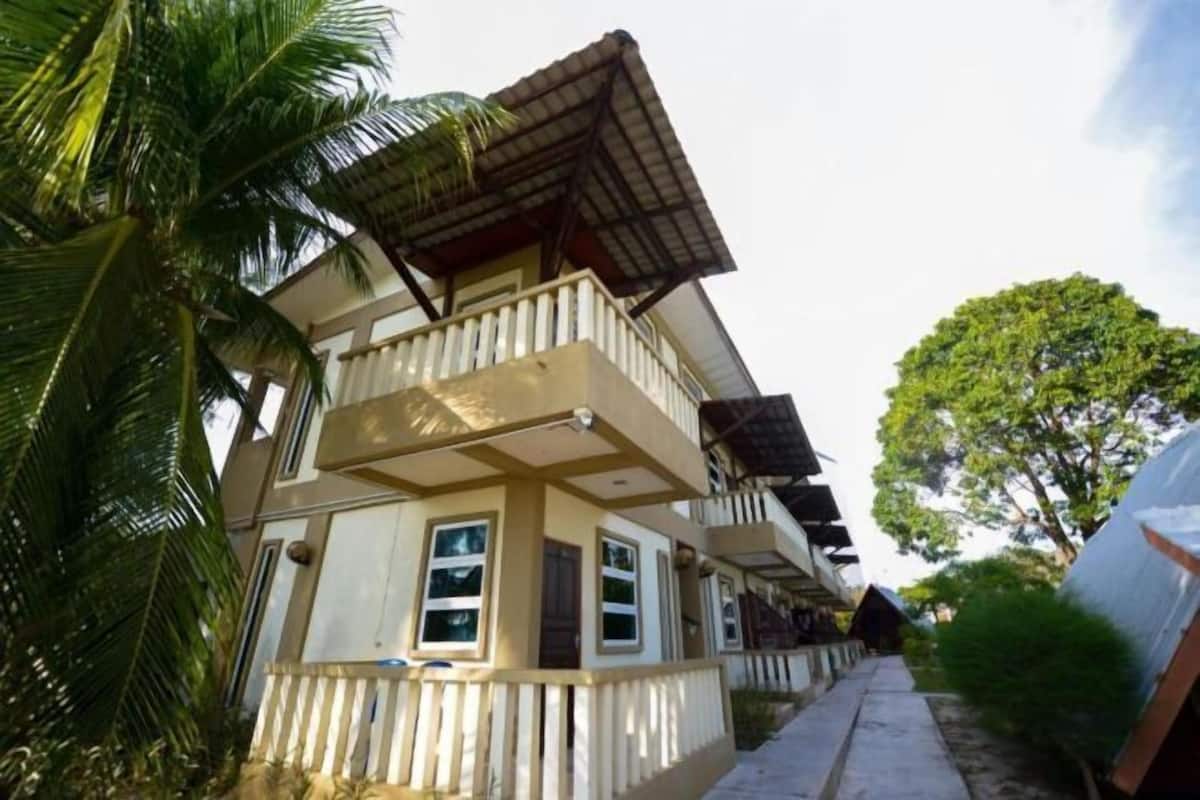 A multi-story building with balconies, a covered walkway, and a palm tree.