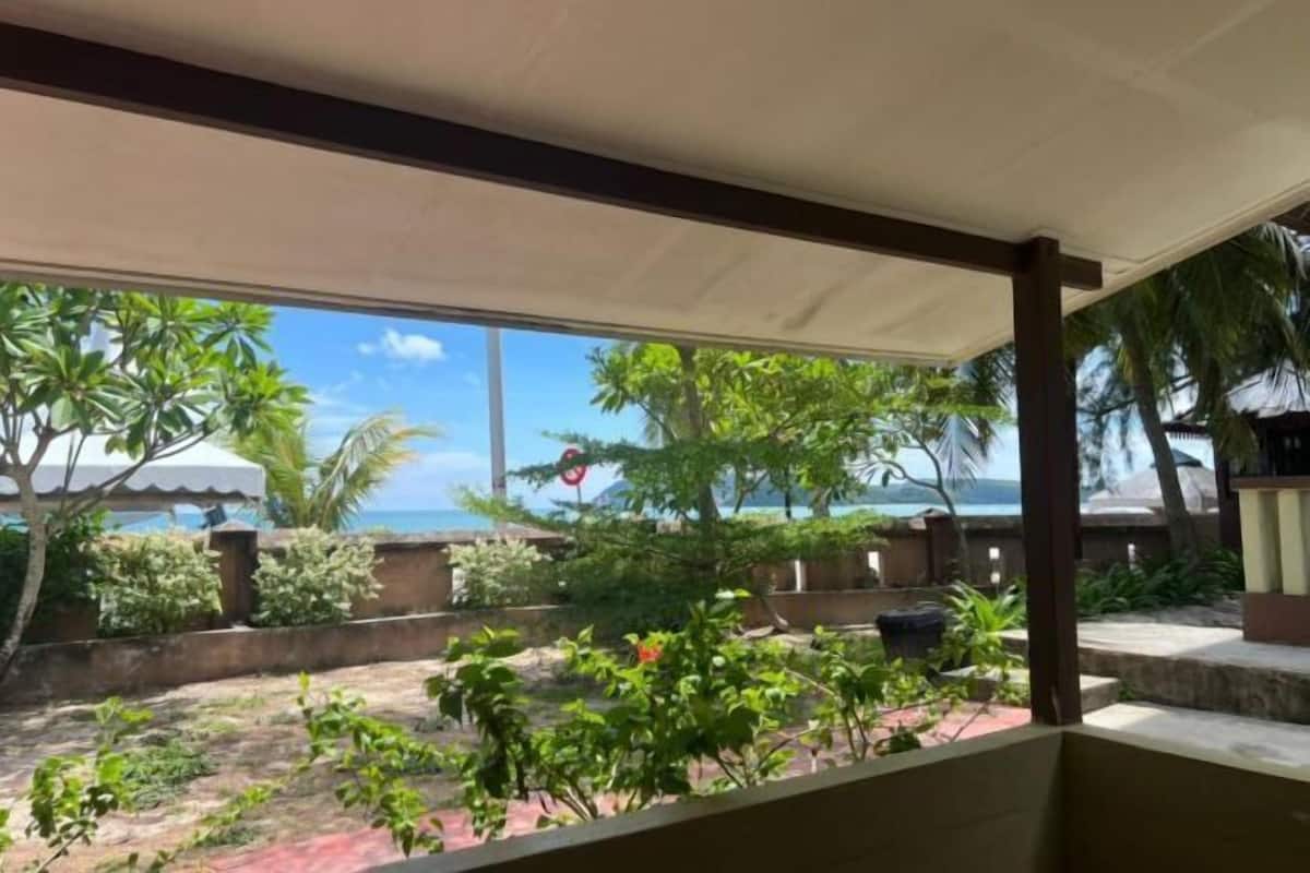 A covered outdoor area with a view of the ocean, surrounded by greenery and a building structure.