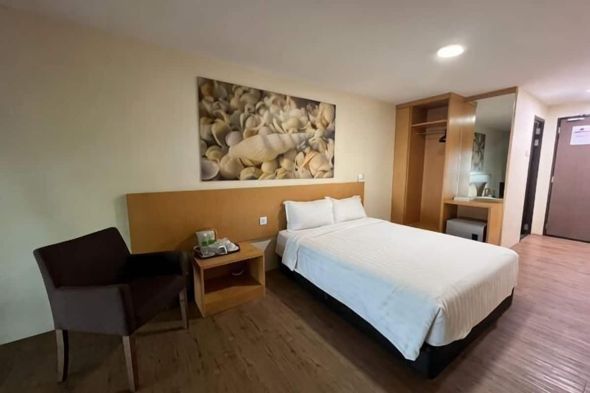A hotel room with a bed, a chair, a nightstand, a painting on the wall, and a wooden floor.