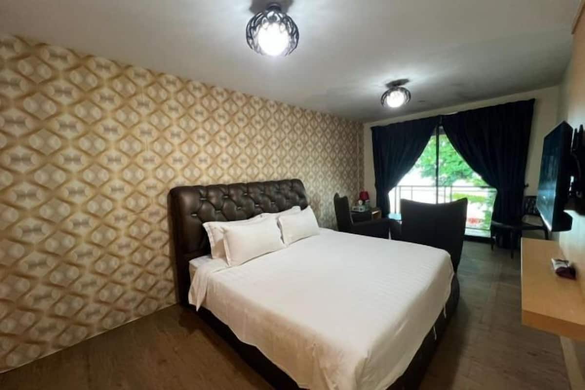 A hotel room with a patterned wallpaper, a large bed, a desk with a chair, and a window with curtains.