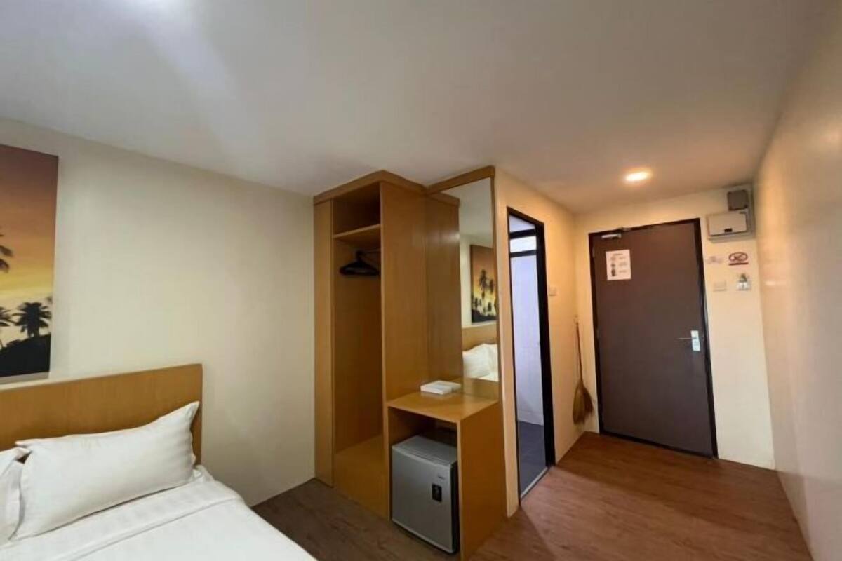A hotel room with a bed, a wooden wardrobe, a small desk, a door, and a wall-mounted air conditioner.