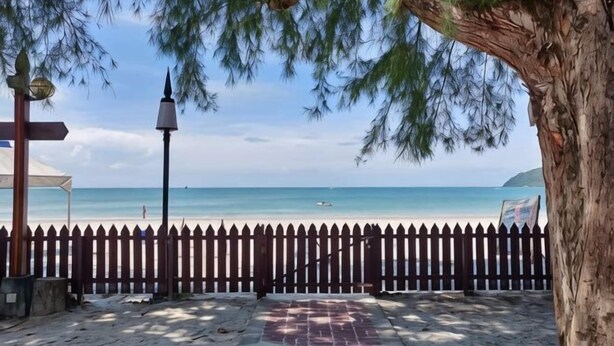 Vista a la playa con una cerca de madera, un farol y un árbol.