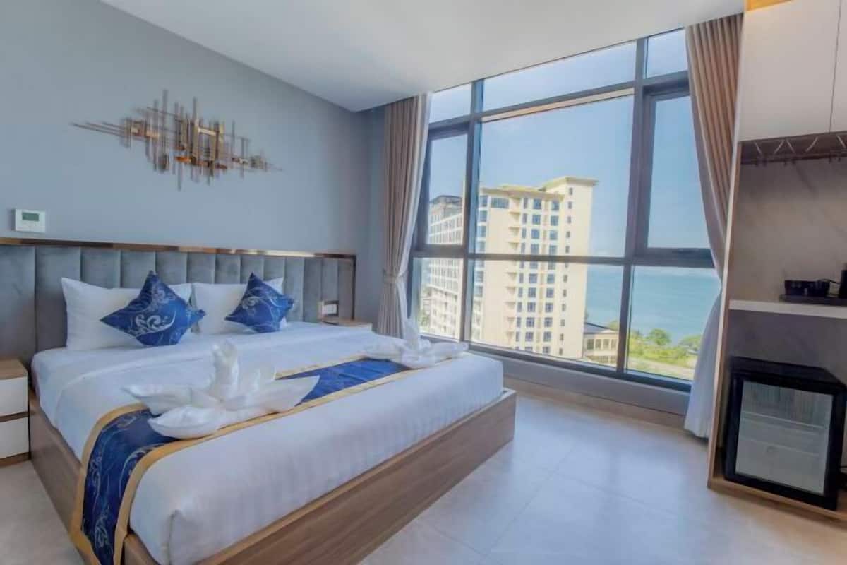 A modern hotel room with a large bed, a view of buildings, and a fireplace.