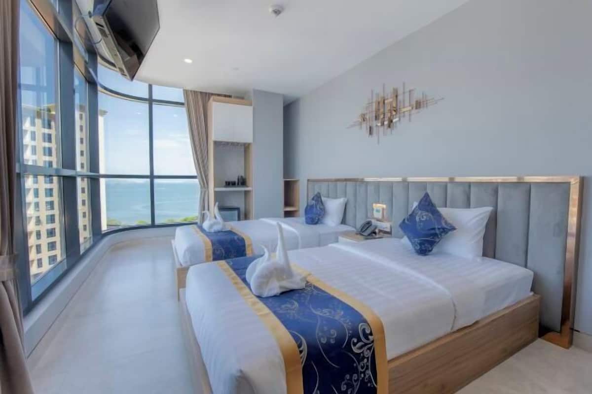 A modern hotel room with two beds, a large window, and a city view.