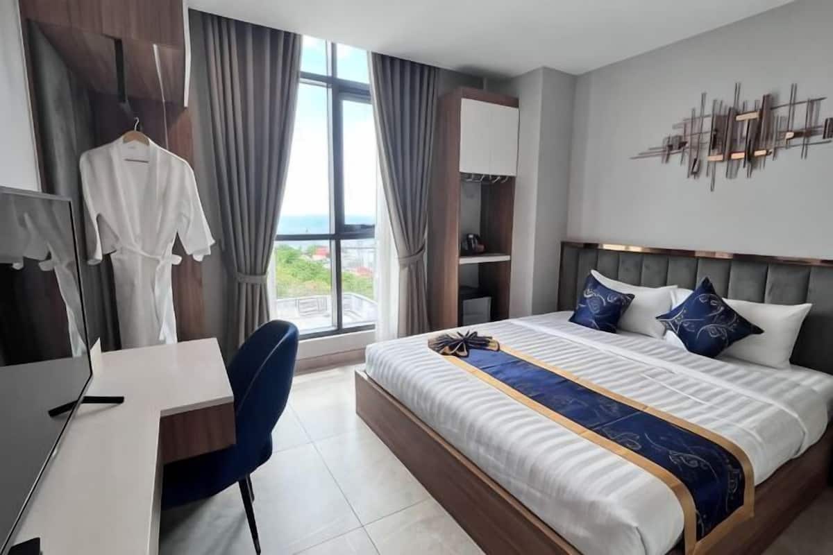 A hotel room with a bed, desk, chair, and a view of the outdoors.