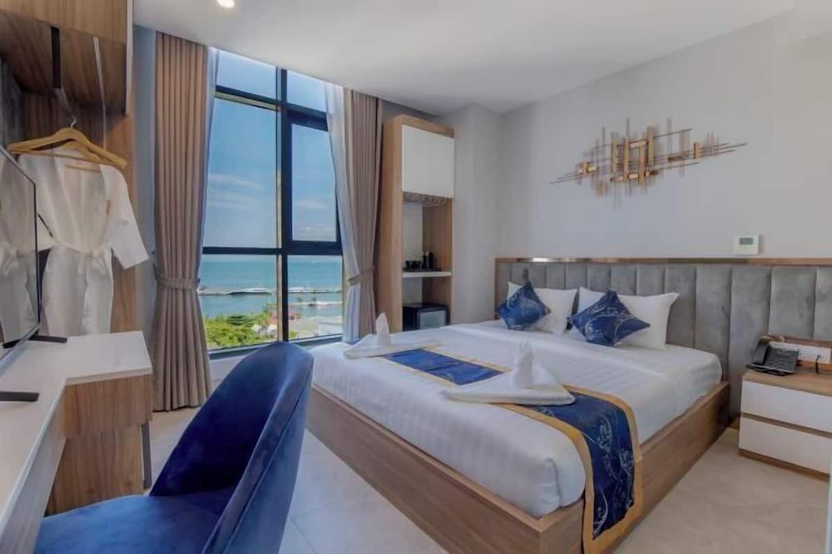 A modern hotel room with a large bed, a desk, and a view of the ocean.
