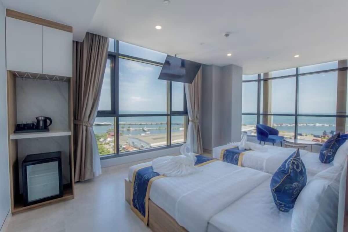 A hotel room with two beds, a TV, a mini-fridge, and a view of the sea.