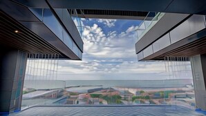 Een moderne hotelkamer met een groot raam, uitzicht op de stad en een geometrisch ontwerp aan het plafond.