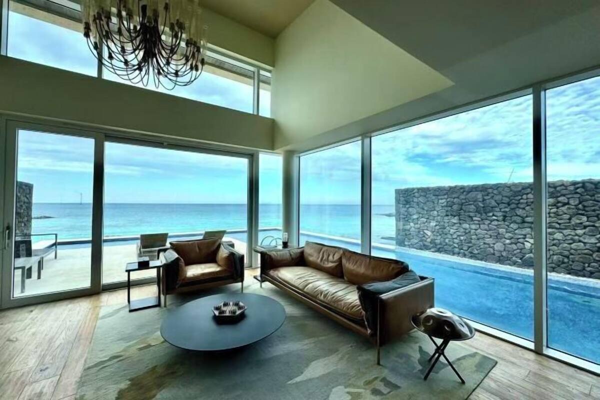 A modern living room with a large window overlooking the ocean, a leather sofa, a coffee table, and a chandelier.
