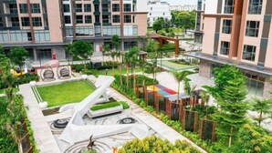 Un hotel moderno con un patio ajardinado que presenta macetas geométricas, una fuente central y un área de descanso con un toldo colorido.