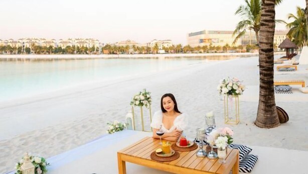 Un montaje para comer en la playa, con una mesa, bebidas y flores.