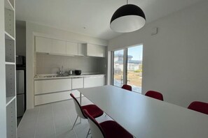 Ett modernt kök med vita skåp, ett stort fönster och en matplats med ett vitt bord och röda stolar.