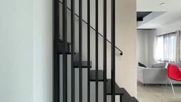 Una escalera moderna con barandales negros y pasamanos, que conduce a una sala de estar con un sofá gris y una silla roja.