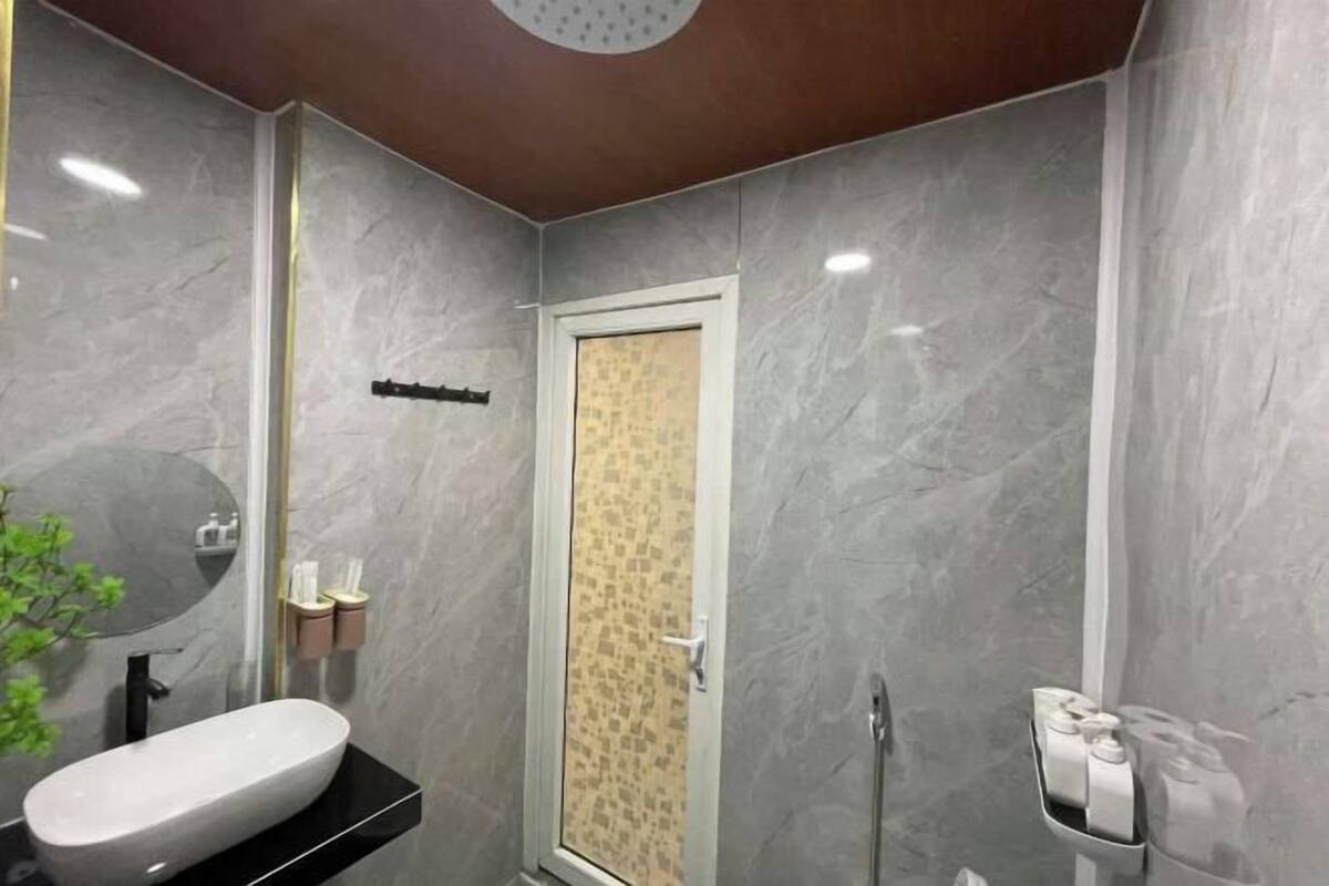 A bathroom with a white sink, a mirror, a shower, and a toilet paper holder.