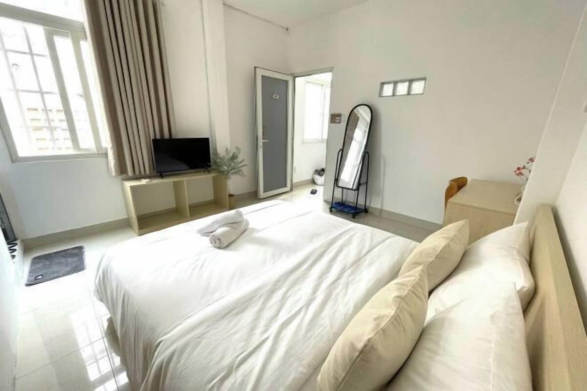 A hotel room with a bed, a TV on a stand, a mirror, and a window with curtains.