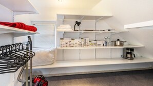 Een kleine kamer met een stapelbed, een stofzuiger, een koffieapparaat en planken met diverse spullen.