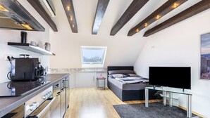 Een moderne keuken met inbouwapparatuur, een eethoek, een bed met televisie en een raam met uitzicht op de stad.