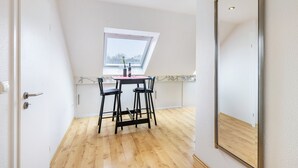 Een kamer met een schuine plafond, een dakraam, een houten vloer, een tafel met stoelen en een grote spiegel.