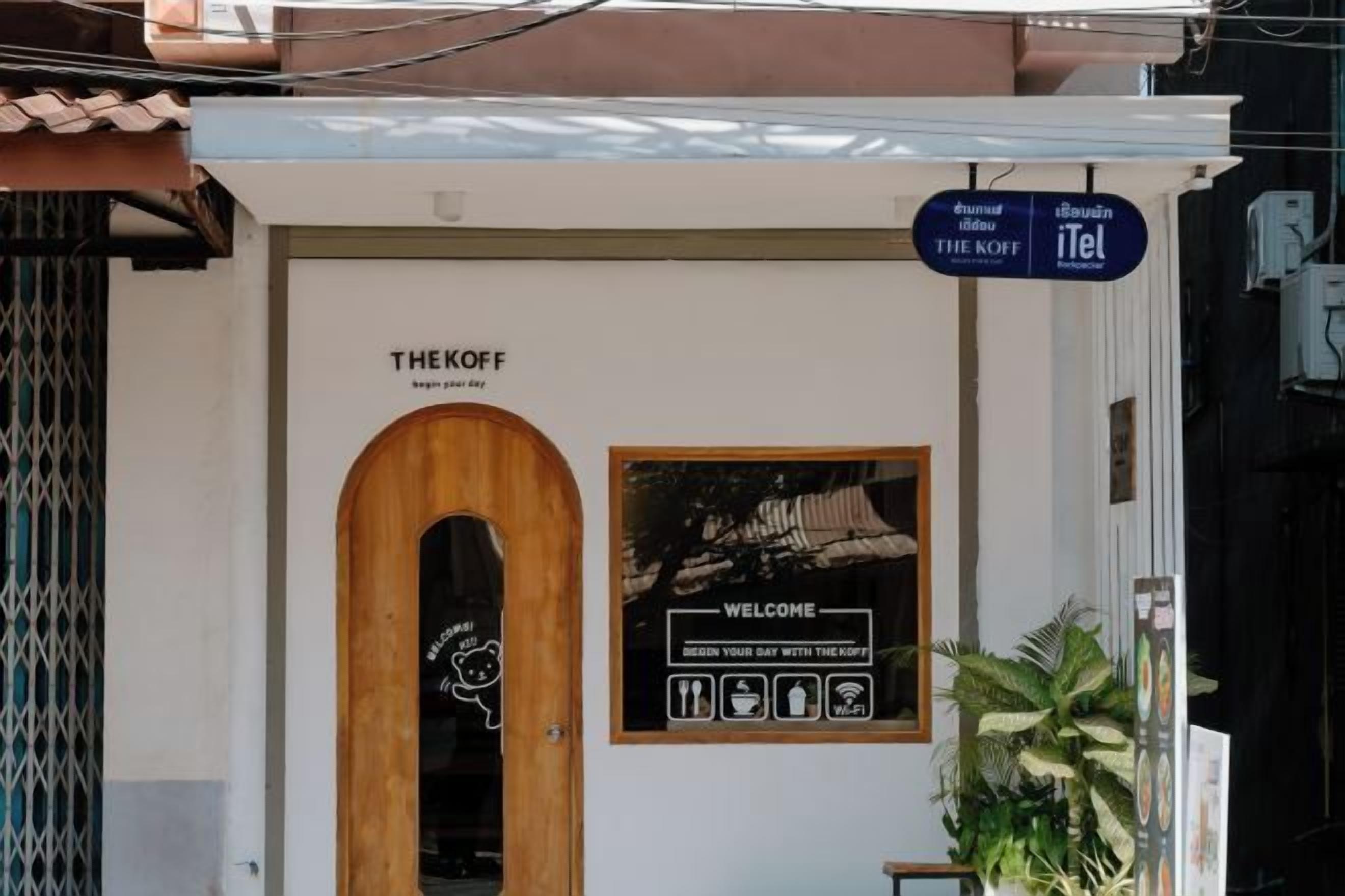 A building entrance with a sign reading "THE KOFF" and a welcome sign with amenities icons.