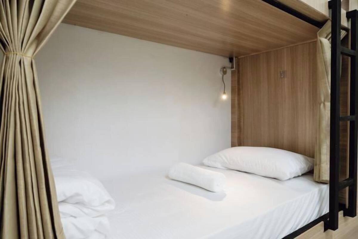 A single bed with white bedding, a wooden headboard, and a curtain.