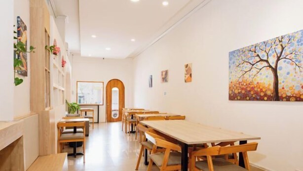 Una habitación amplia con mesas y sillas de madera, un cuadro grande en la pared y una puerta de madera al fondo.