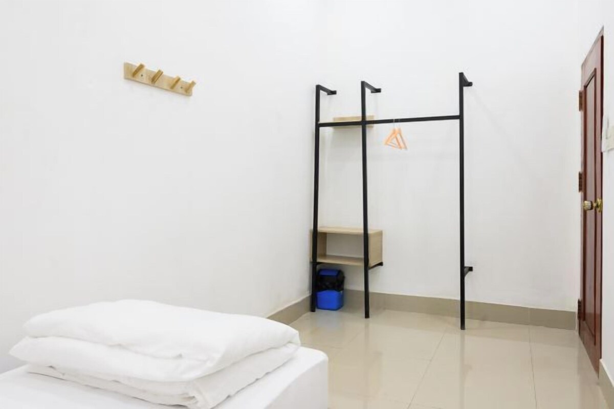 A hotel room with a bed, a small shelf unit, a hanging rack, and a door.