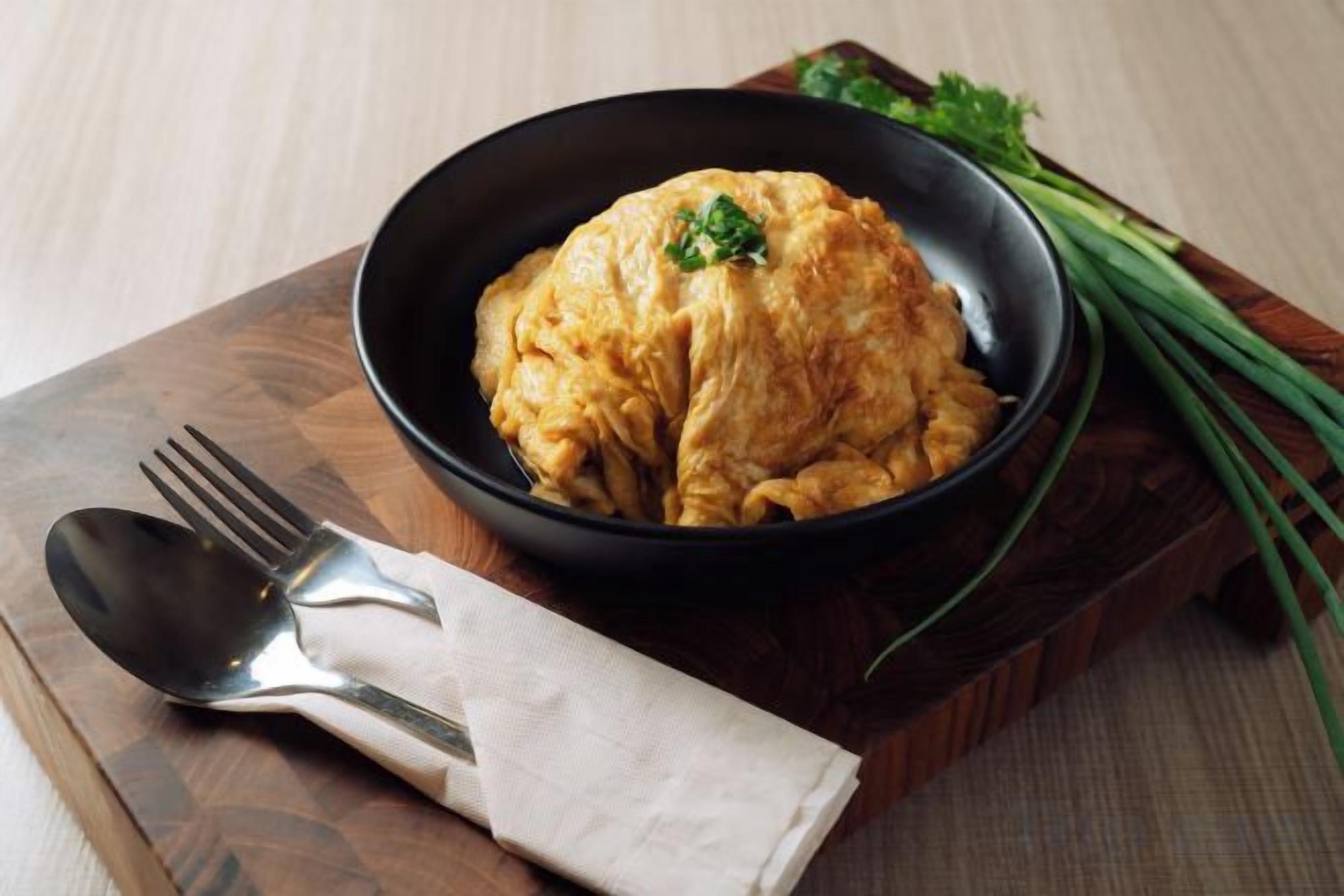 A bowl of food on a wooden board with a fork and spoon beside it.
