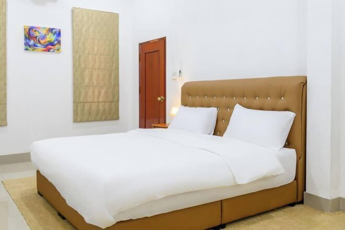 A bed with a brown headboard, white bedding, and a beige rug.