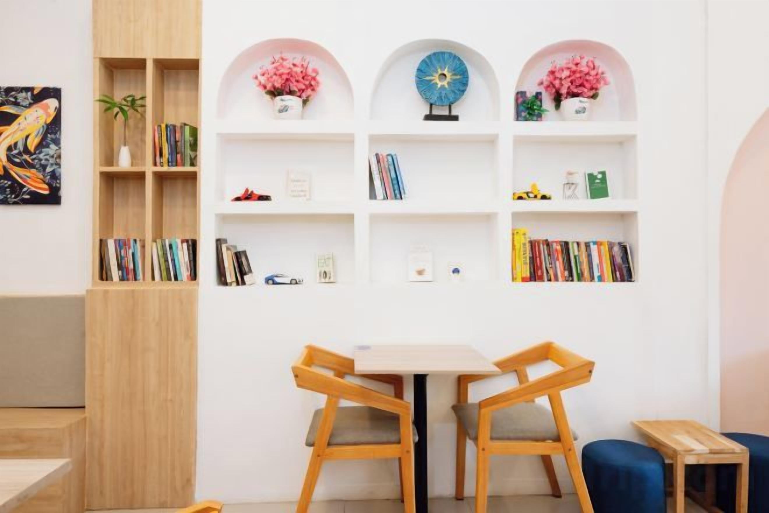 A room with a white wall, a wooden bookshelf, a round table with chairs, and a small blue sofa.