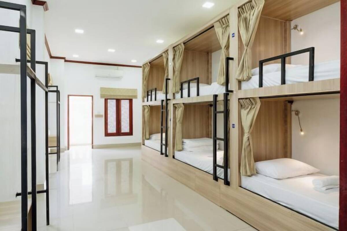 A hotel room with bunk beds, a wooden floor, a door, and a window.