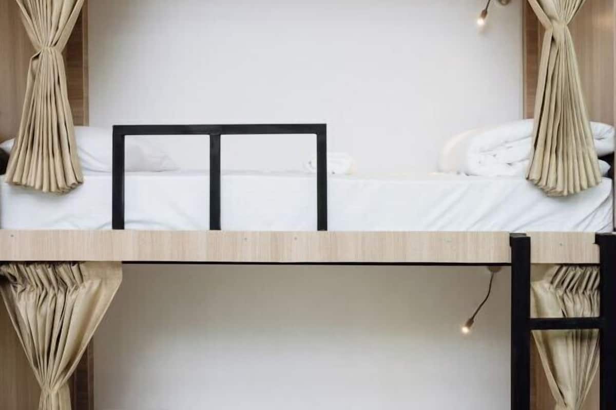 A bunk bed with a wooden frame, white bedding, and beige curtains.