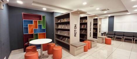 A library with bookshelves, a round table, and orange seating.