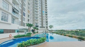A swimming pool with a view of a high-rise building, surrounded by greenery. - Apartment kulai (Kulai)