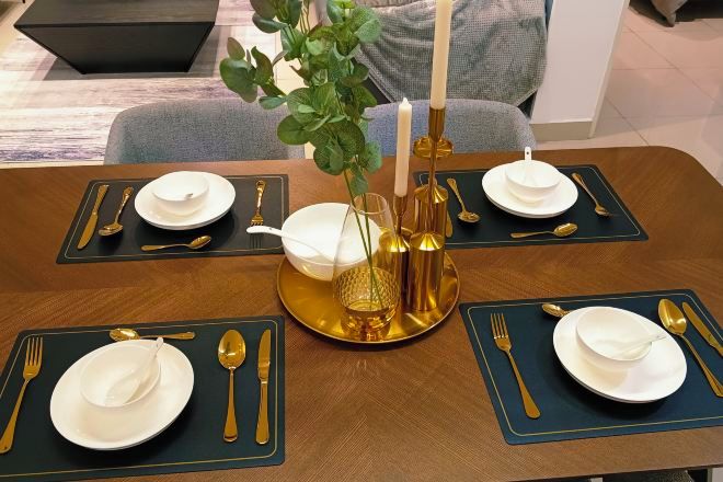 A dining table set with gold and white tableware, a vase with green foliage, and candles.
