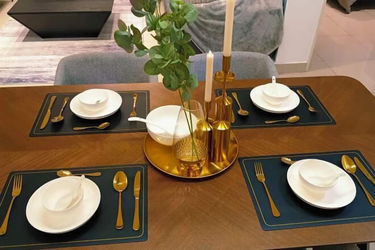 A dining table set with gold and white tableware, a vase with green foliage, and candles.